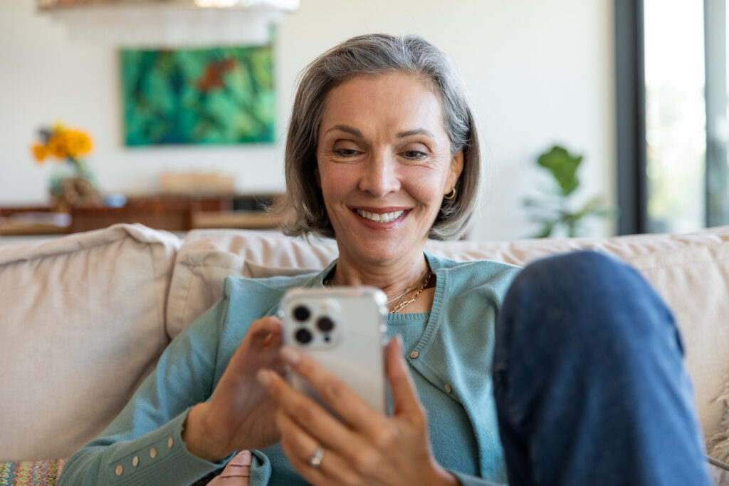 An older woman smiles at her cell phone while relaxing.