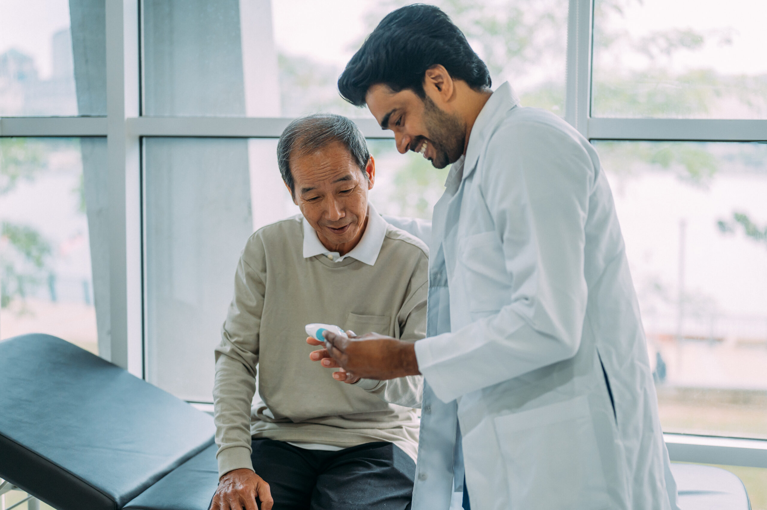 Smiling male doctor discussing over medical record with senior man in hospital